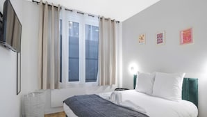 A bedroom with a bed, curtains, a TV, a wall-mounted light, and framed pictures.