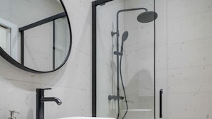 A modern bathroom with a white sink, a round mirror, and a glass-enclosed shower.
