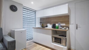 Una cocina compacta con microondas integrado, cafetera y un refrigerador pequeño.