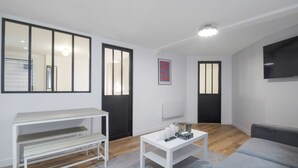 Una sala de estar moderna con un sofá, una mesa de centro blanca, un banco y un televisor montado en la pared.