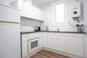 Moderni keittiö, jossa on valkoiset kaapit, musta työtaso, sisäänrakennettu uuni, kahvinkeitin ja vedenkeitin.