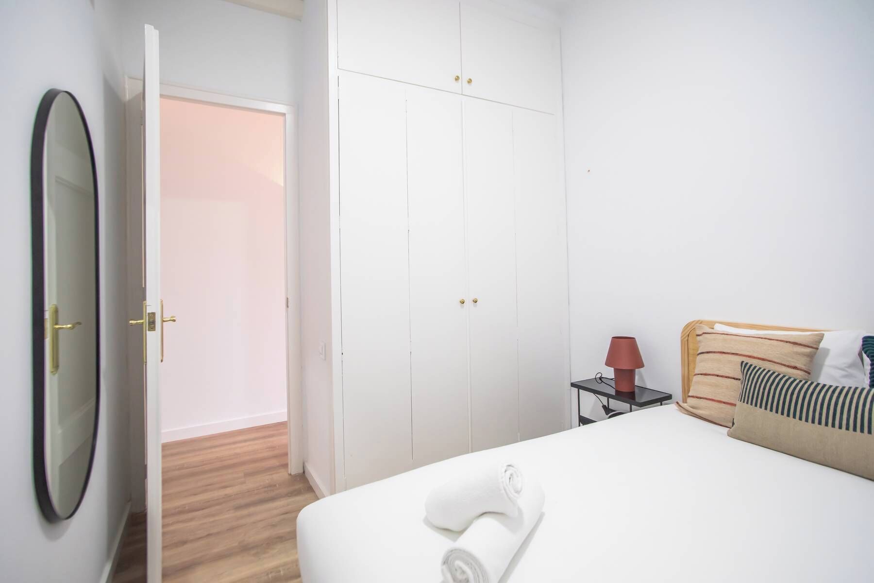A hotel room with a bed, a bedside table with a lamp, a mirror, and a wardrobe.