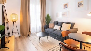 Ein modernes Wohnzimmer mit einem grauen Sofa, zwei Beistelltischen, einem Couchtisch und einem Essbereich mit Stühlen.