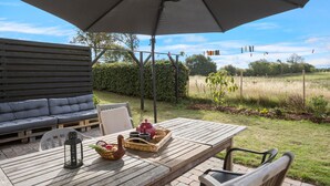Un patio al aire libre con una mesa de madera, un banco acolchado y una sombrilla.