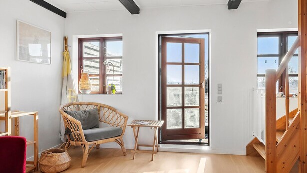 Una habitación acogedora con un ventanal grande, una silla de mimbre, una mesita pequeña y una silla roja.