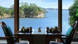A dining table with chairs facing a scenic view of a body of water and a rocky island.