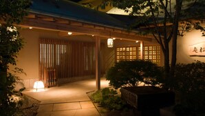 A traditional Japanese-style entrance with a wooden gate, a lantern, and a stone pathway leading to a covered area.