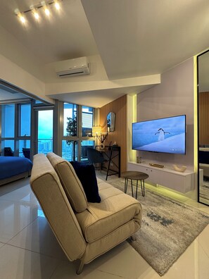 A modern living room with a sofa, a coffee table, a TV, and a view of the city. - Stylish Comfort & Ultimate Convenience: Your Go-To in BGC. (Taguig)
