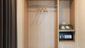 A walk-in closet with wooden shelving, a hanging rack, and a microwave on the lower shelf. - Good Nine Hotel (Bang Bo)
