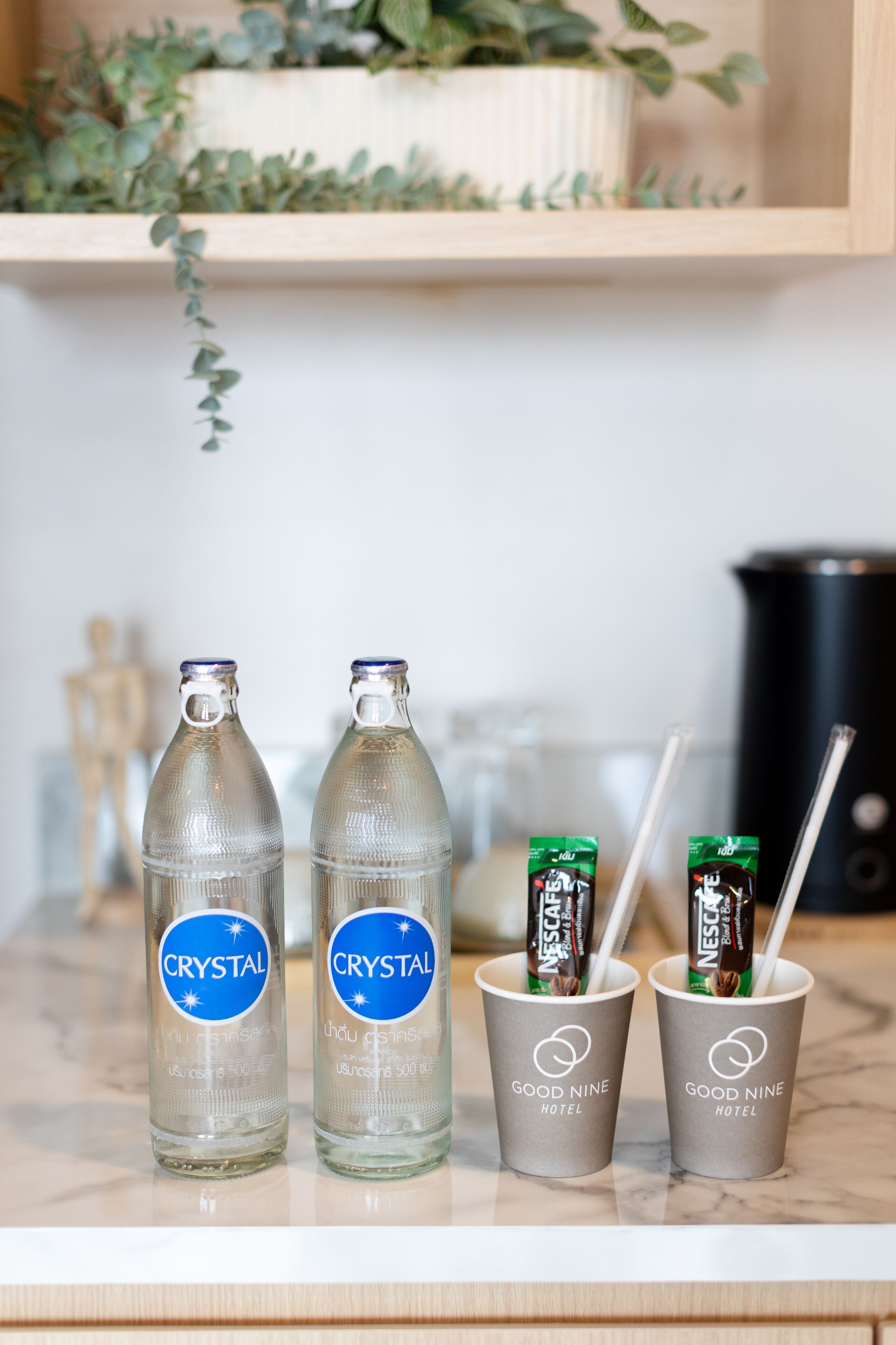 Twee flessen Crystal water en twee bekers met Nescafé en het logo van Good Nine Hotel.