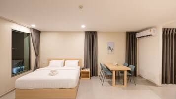 A hotel room with a bed, bedside table, desk, chairs, and an air conditioning unit.