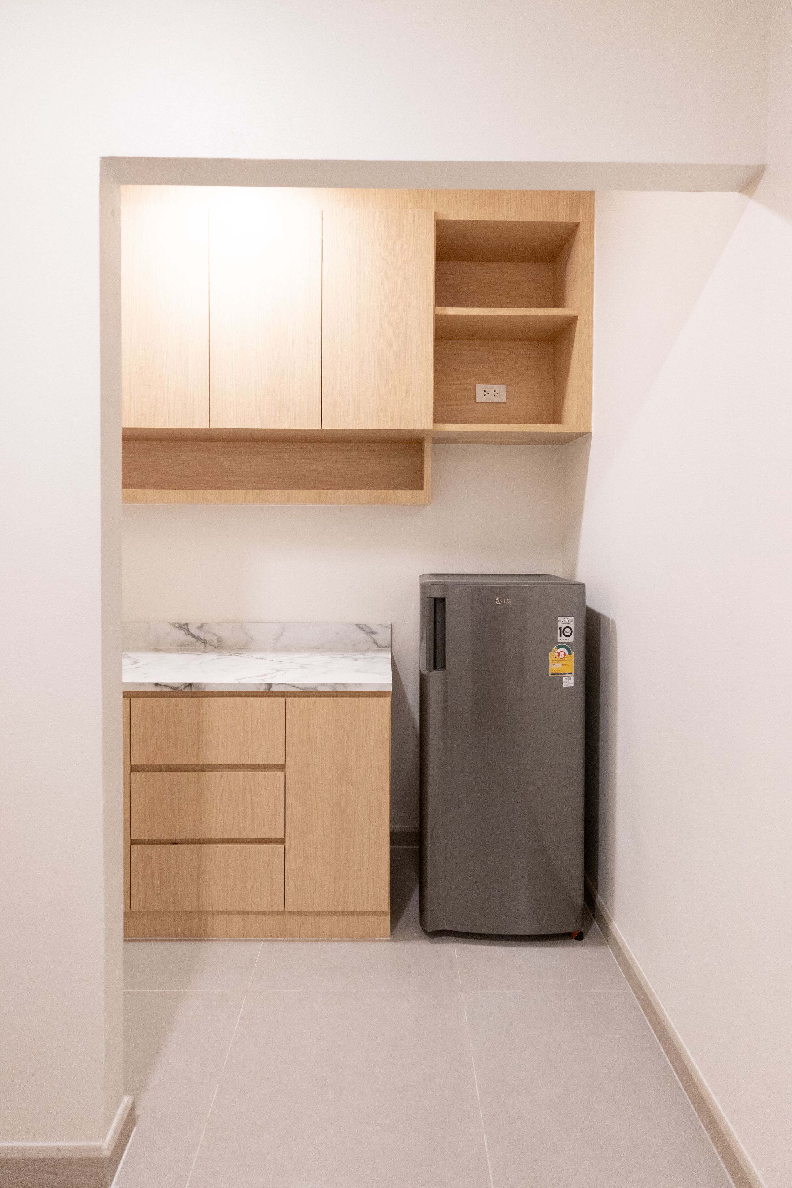 Una cocina compacta con armarios de madera, encimera de mármol y refrigerador empotrado.