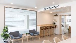 A modern reception area with a glass wall, a reception desk, two bar stools, and a seating area with chairs and a small table. - Good Nine Hotel (Bang Bo)