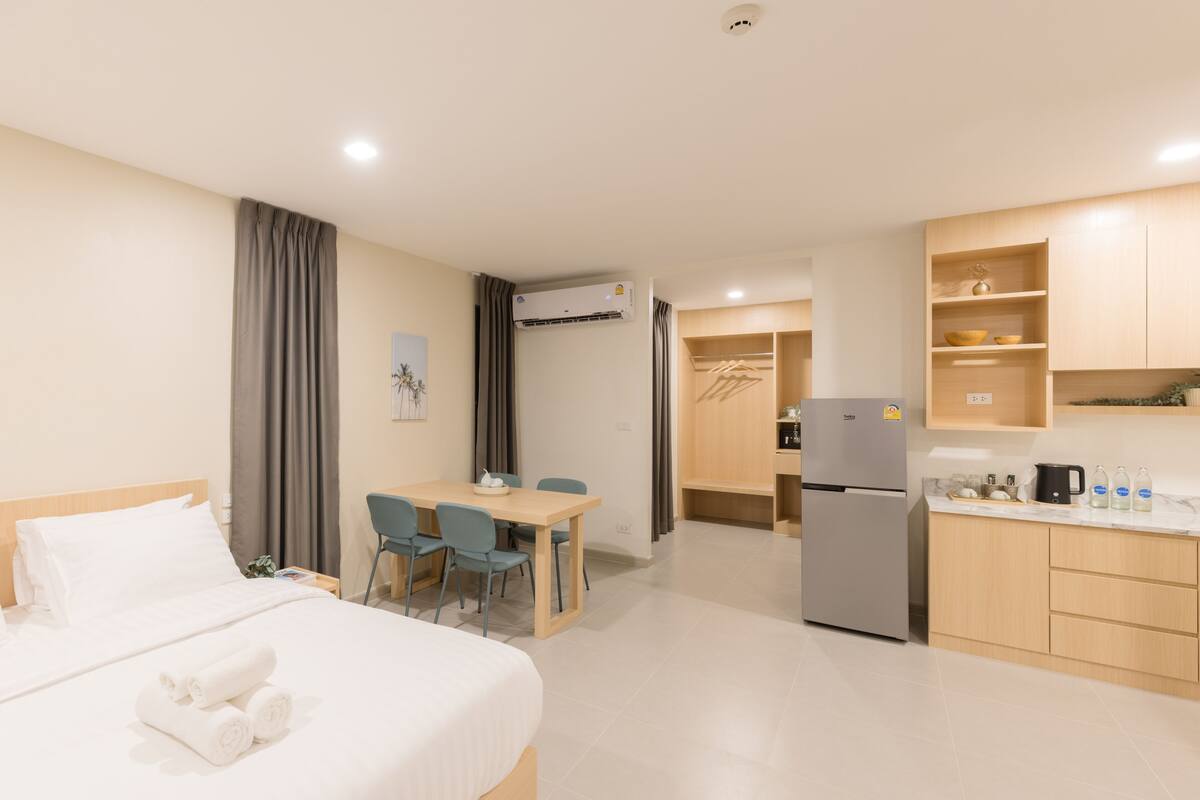 A hotel room with a bed, a desk, chairs, a kitchenette, and a bathroom.