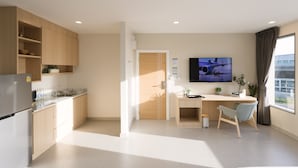 A modern kitchen with a refrigerator, sink, and wooden cabinets. There is a dining area with a table and chairs, and a TV mounted on the wall. - Good Nine Hotel (Bang Bo)