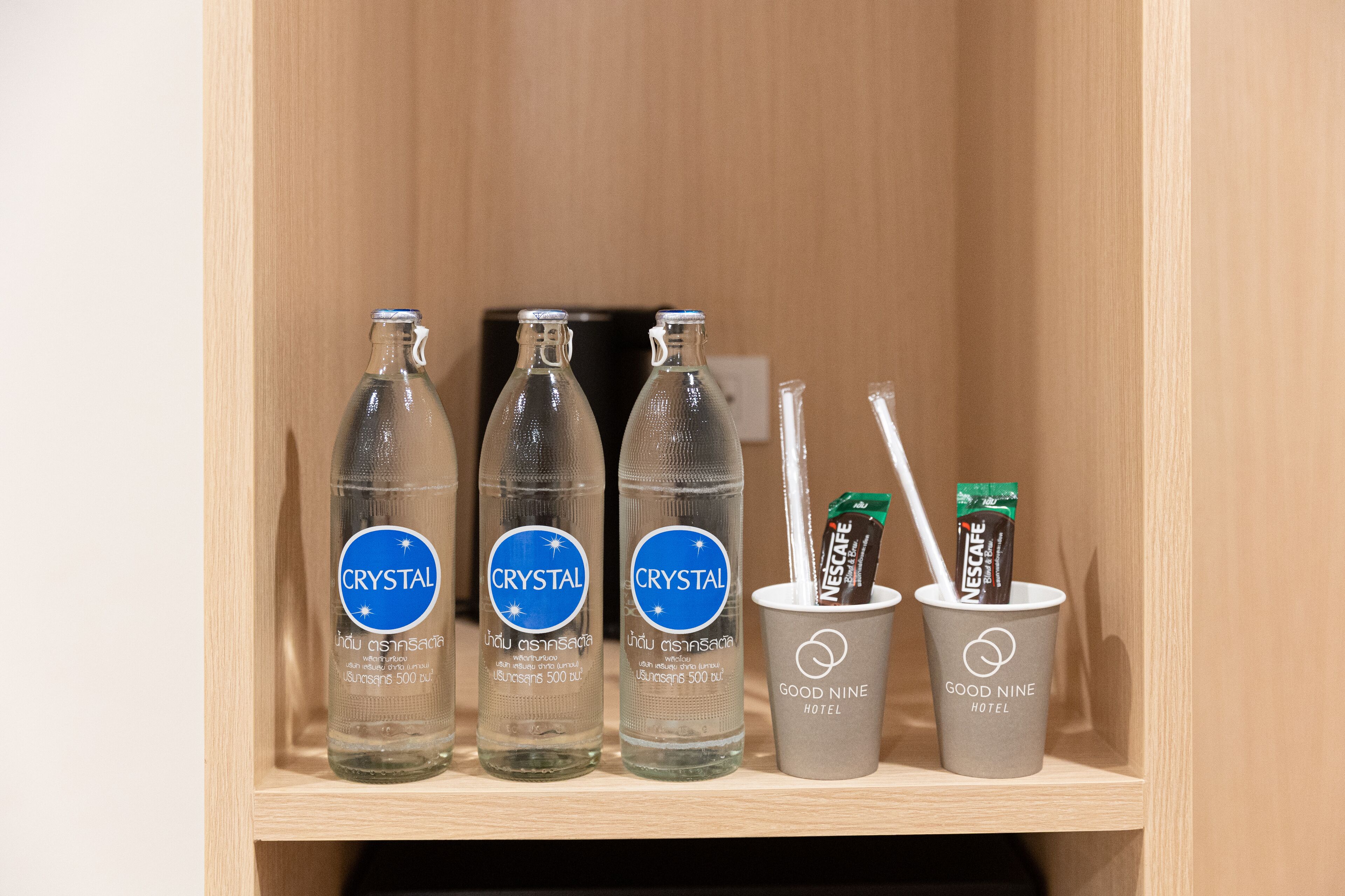 A shelf with three bottles of Crystal water and two cups of Nescafe in a Good Nine Hotel setting.