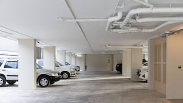 Un parcheggio multipiano con diverse auto parcheggiate, pareti bianche e tubature a vista sul soffitto.
