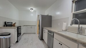 Een moderne keuken met witte kasten, een roestvrijstalen koelkast, een vaatwasser en een spoelbak met een kraan.