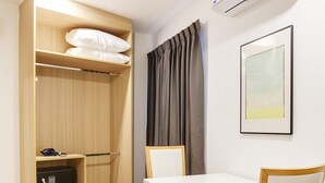 A room with a wooden wardrobe, a white table with chairs, an air conditioner, and a framed picture on the wall. - TAKKA Hotel (Bangkok)