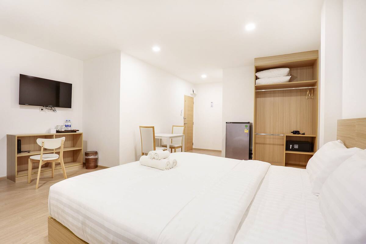 Habitación de hotel con cama, escritorio, silla, televisor, armario y una pequeña mesa.