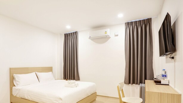 A hotel room with a bed, a desk, a chair, an air conditioner, and a TV. - TAKKA Hotel (Bangkok)