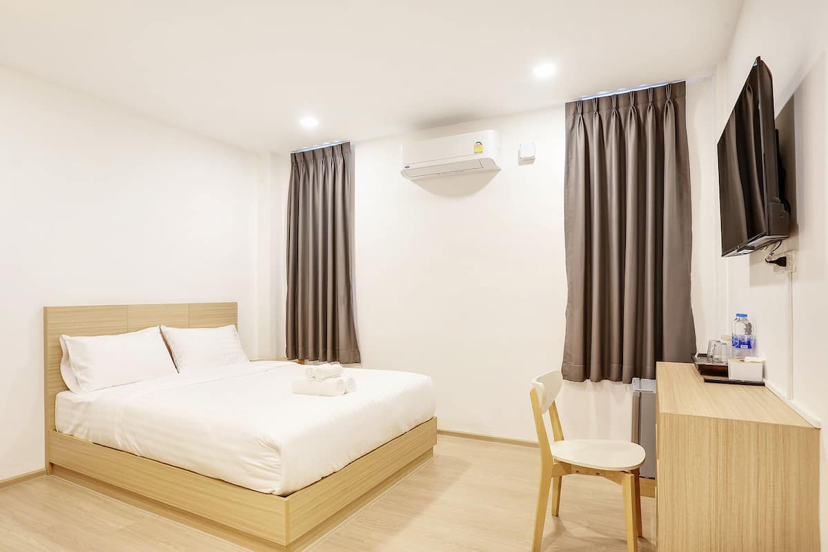Una habitación de hotel con cama, escritorio, silla, aire acondicionado y televisor.