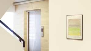 An elevator with a digital display, a framed artwork on the wall, and a staircase with a black handrail. - TAKKA Hotel (Bangkok)