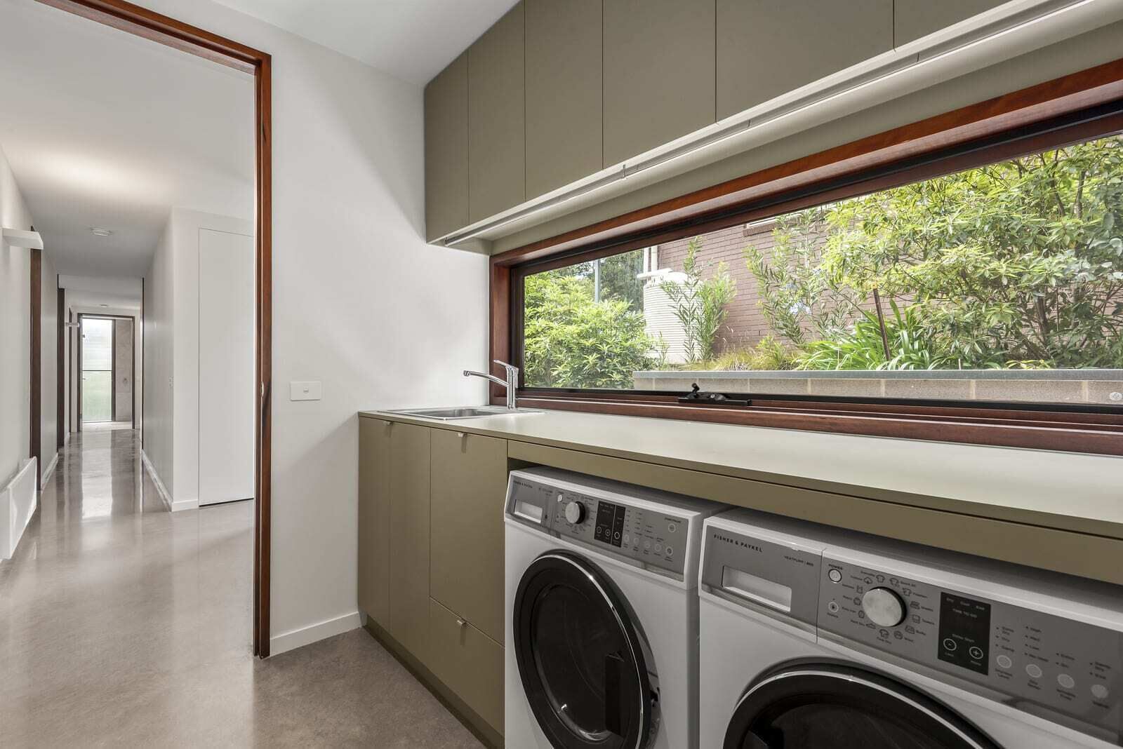 A modern kitchen with a built-in washer and dryer, a window with a view of greenery, and a hallway leading to another room.