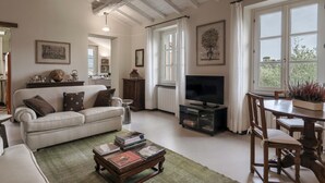 Een woonkamer met een witte bank, een salontafel met boeken, een televisie en een eethoek met een tafel en stoelen.
