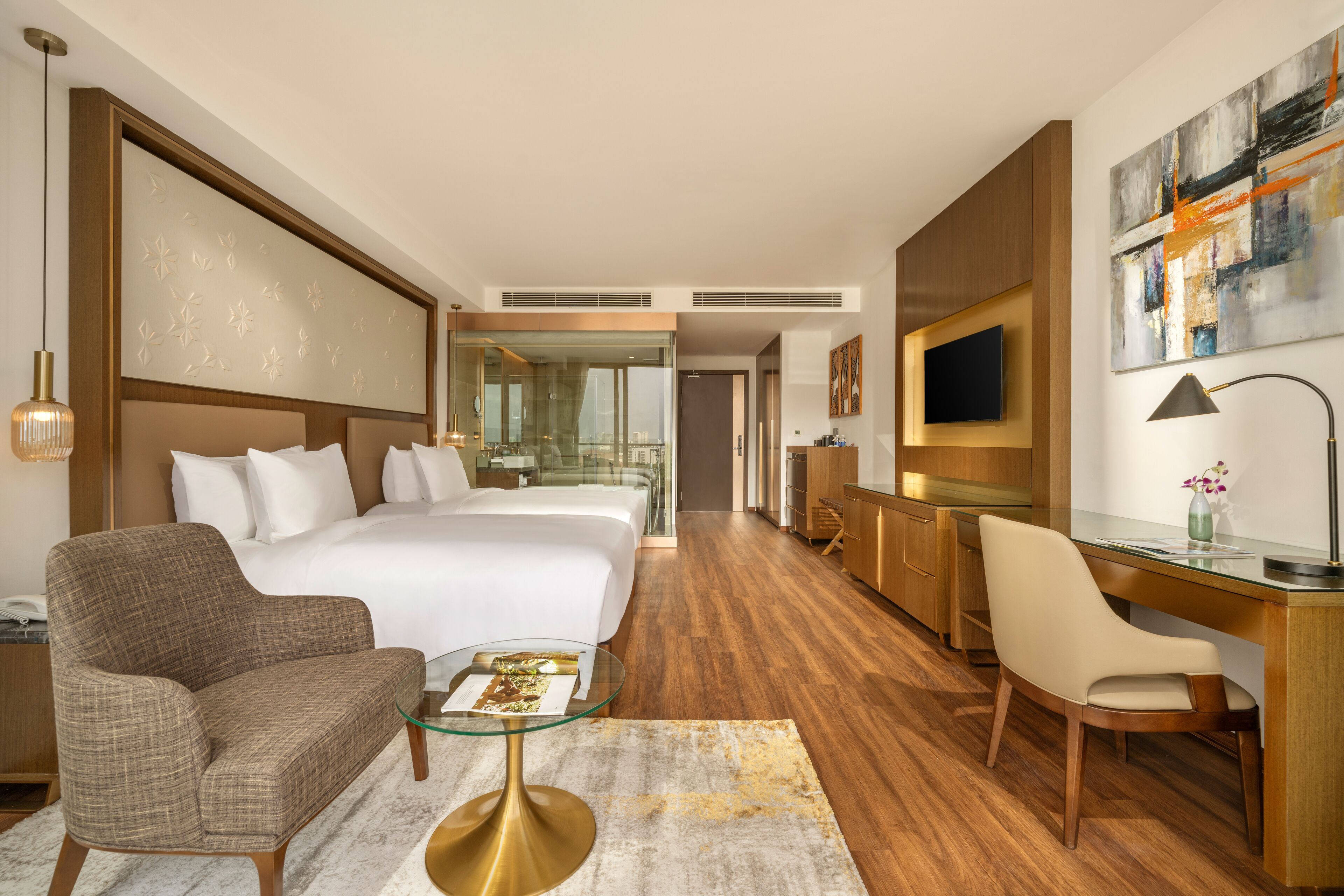 A modern hotel room with a large bed, a desk, a chair, a sofa, and a television.