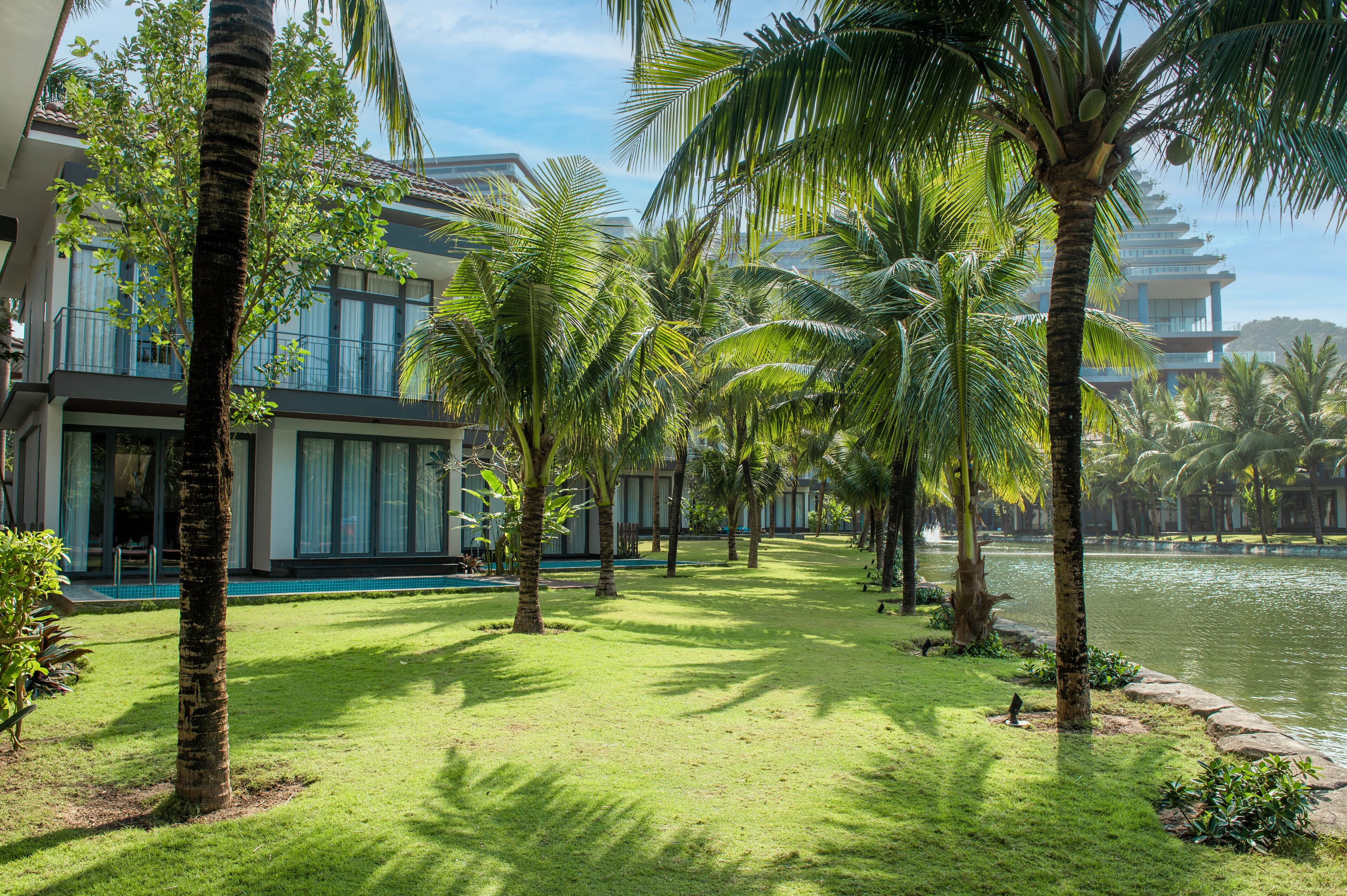 Un resort con piscina, palmeras y un edificio con amplios ventanales.