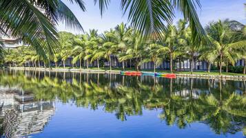 A tranquil water body reflecting palm trees and a building with a balcony.