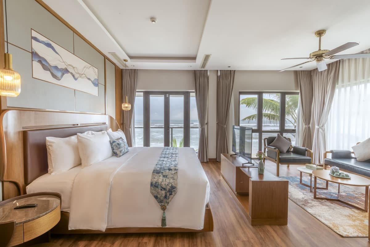 Une chambre d’hôtel moderne dotée d’un grand lit, d’une télévision, d’un coin salon et d’un balcon offrant une vue sur l’océan.