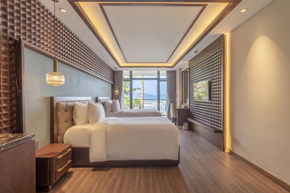 Une chambre d’hôtel moderne avec un grand lit, un parquet en bois et une vue sur la mer grâce à de grandes fenêtres.