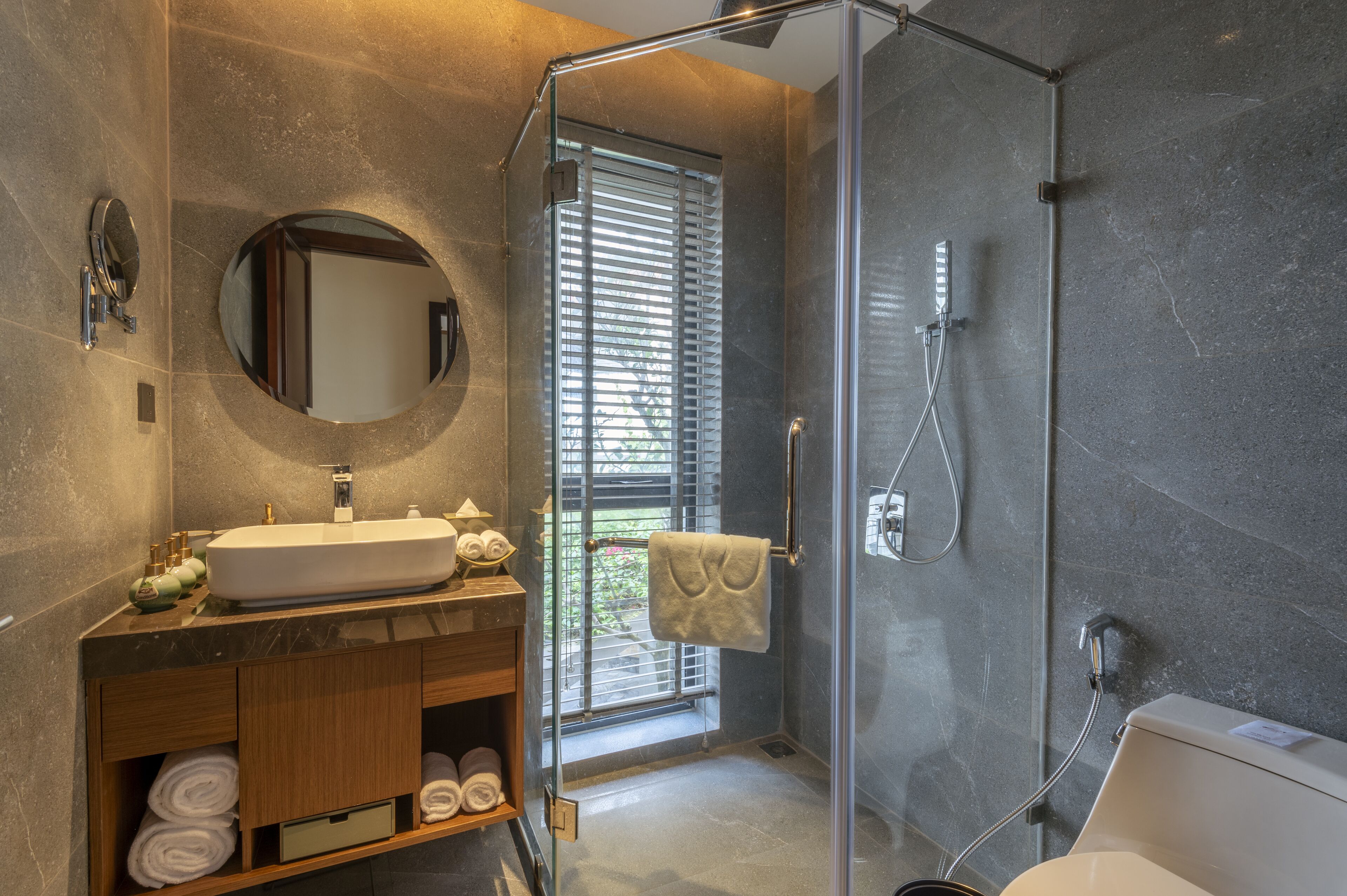 A modern bathroom with a glass-enclosed shower, a round mirror, and a vanity with a sink and towel storage.