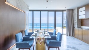A dining area with a view of the ocean, featuring a long table with blue chairs, a patterned tablecloth, and a modern kitchen in the background. - KOI Resort & Residence Da Nang - Inclusive Spa access (Da Nang)