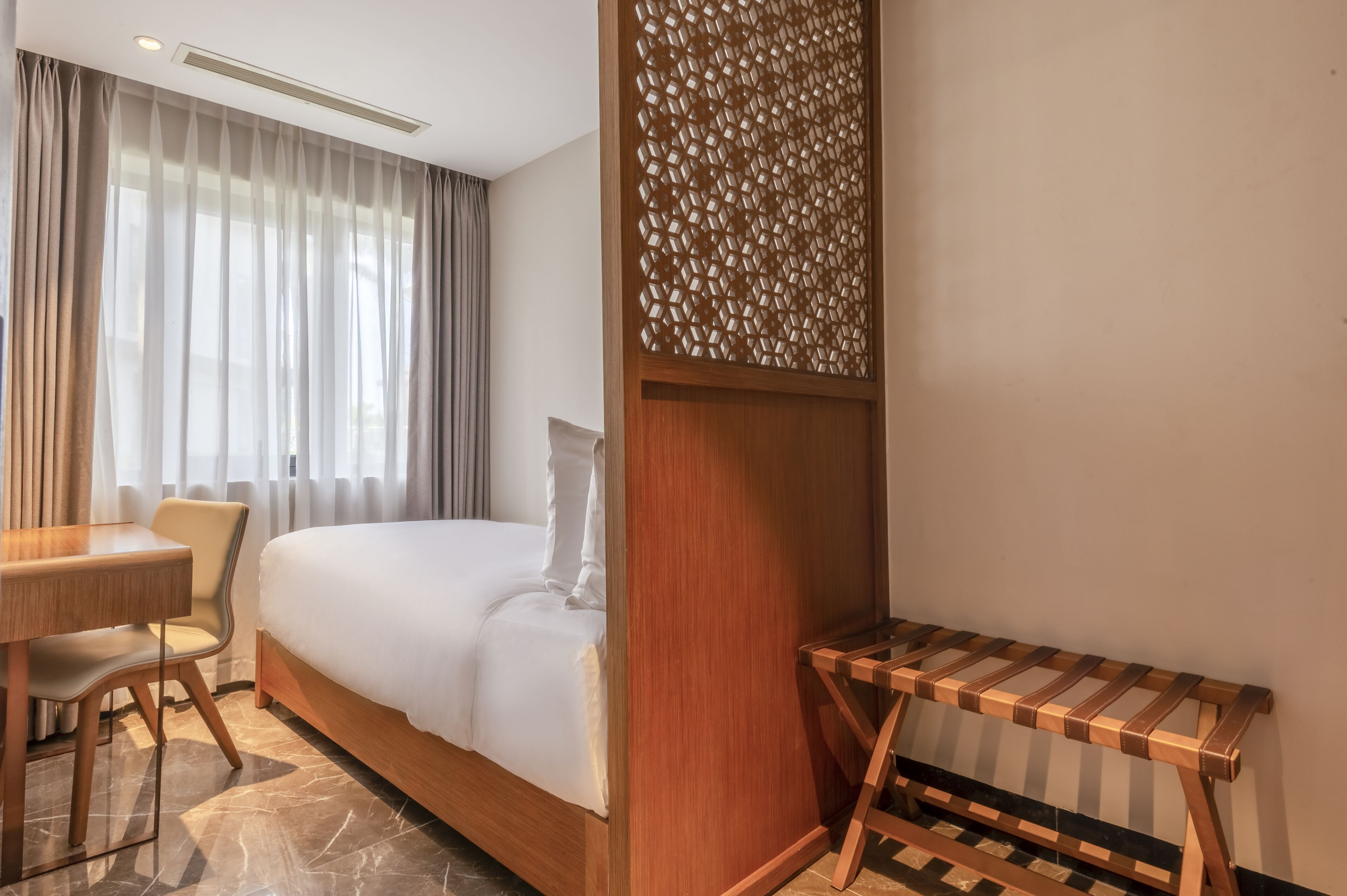 A hotel room with a bed, a desk, a chair, and a small table.