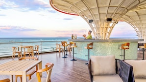 A deck with wooden tables and chairs, a bar area, and a view of the ocean. - KOI Resort & Residence Da Nang - Inclusive Spa access (Da Nang)