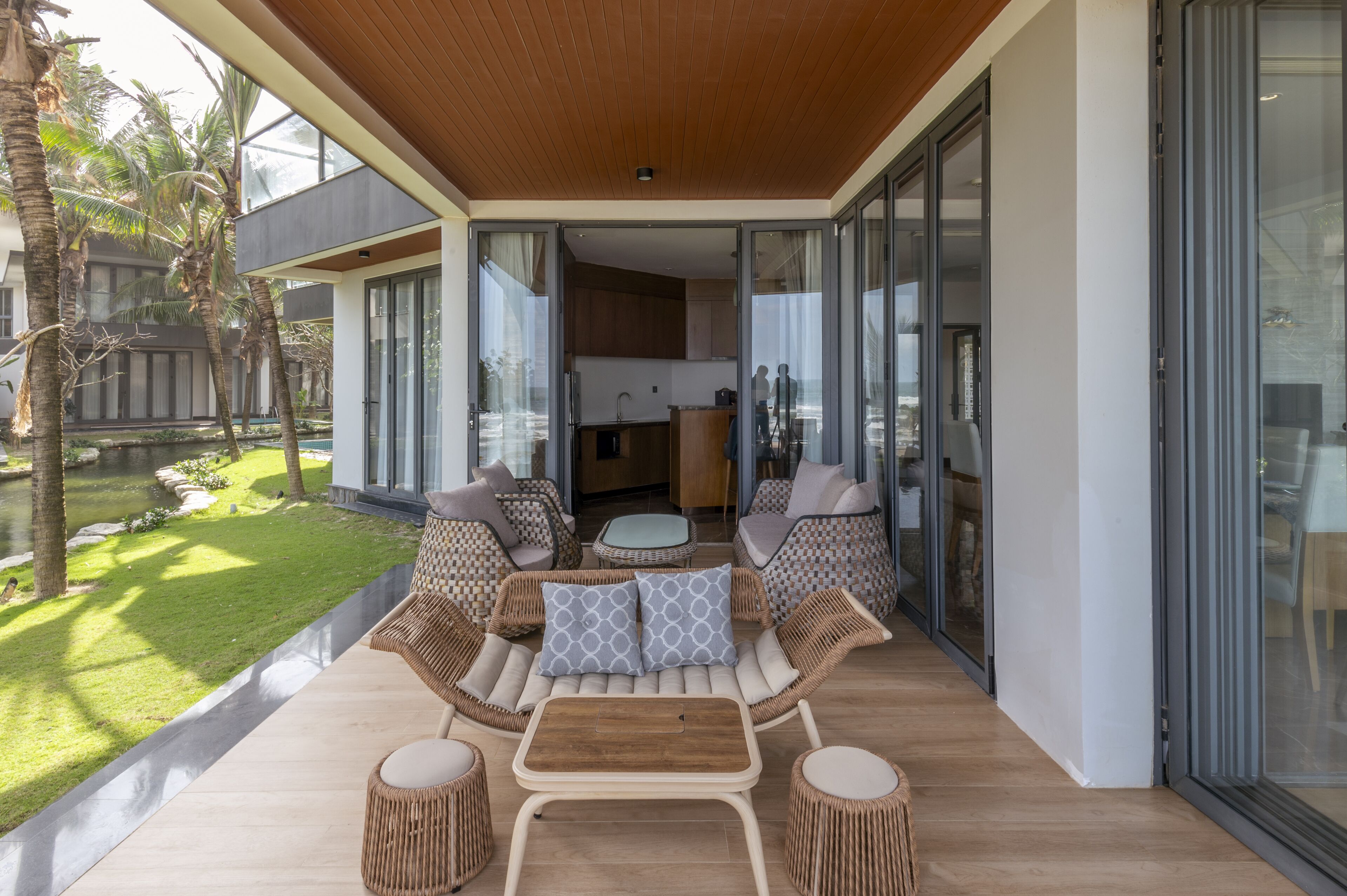 A modern outdoor seating area with wicker furniture and a wooden table, overlooking a well-maintained garden and a residential building.
