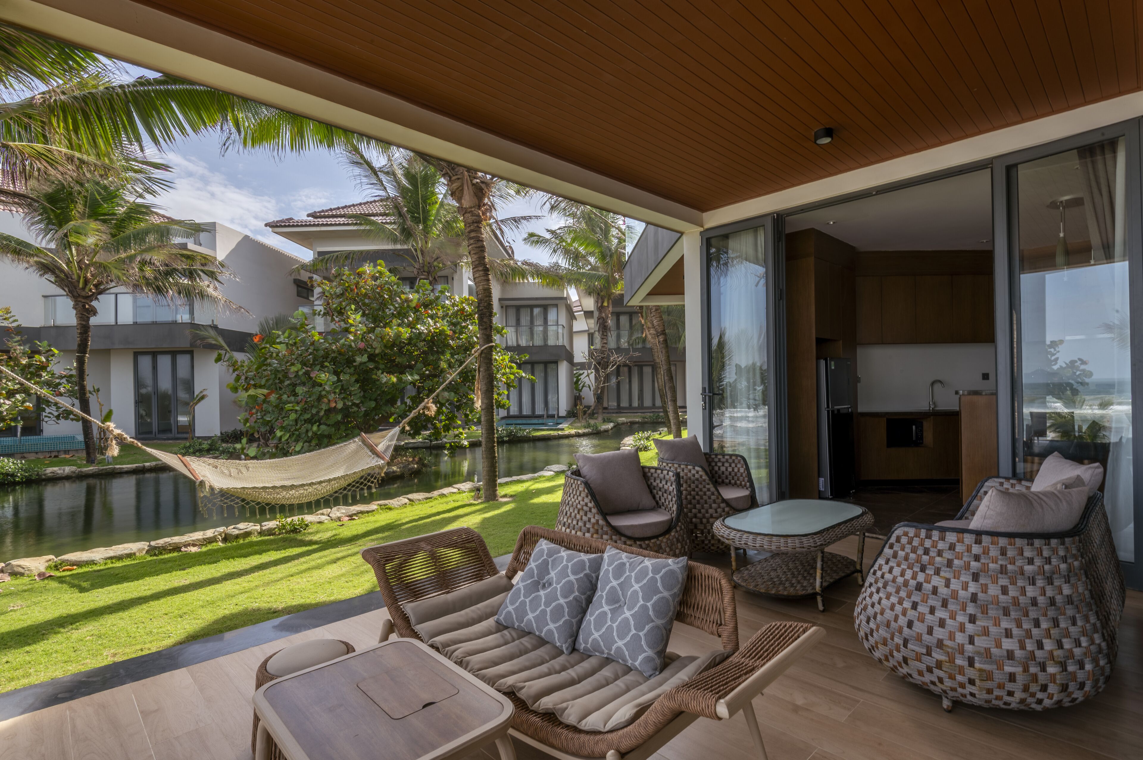 A modern outdoor living area with wicker furniture, a hammock, and a view of a pool and neighboring buildings.