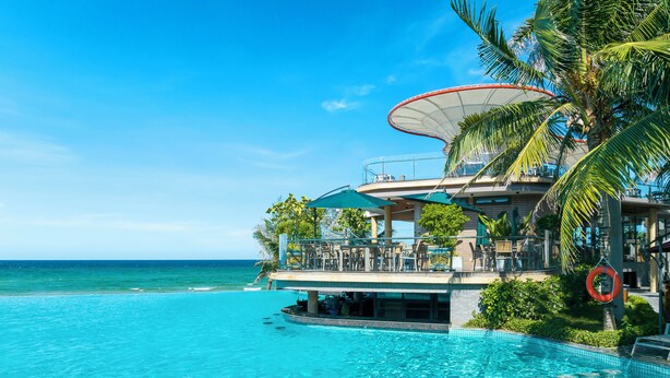 A resort pool with clear blue water, a palm tree, and a building with outdoor seating. - KOI Resort & Residence Da Nang - Inclusive Spa access (Da Nang)