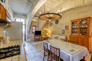 A stone-walled room with a kitchen area, a dining table, and a wooden cabinet.