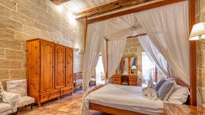 A bedroom with a wooden bed, white curtains, a stone wall, and a wooden wardrobe. - Ta'leli Pool Farmhouse in Gozo (Gharb)