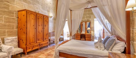 A bedroom with a wooden bed, white curtains, a stone wall, and a wooden wardrobe.