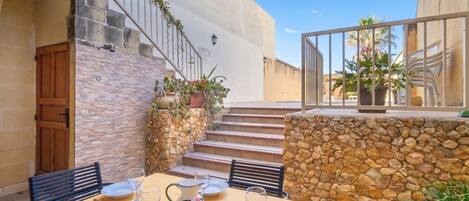 Un área de comedor al aire libre con paredes de piedra, una puerta de madera y una escalera que sube a un nivel superior.