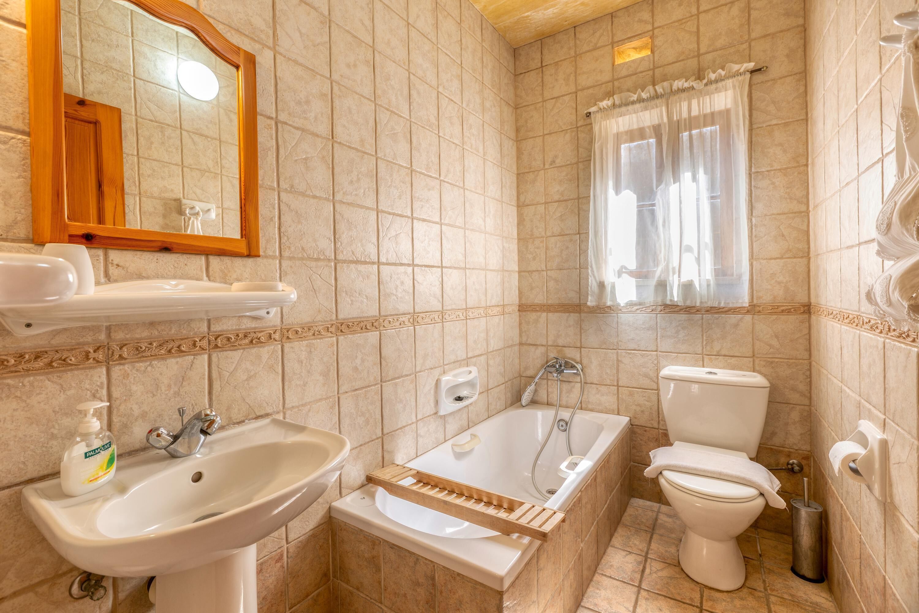A bathroom with a sink, mirror, bathtub, toilet, and window with curtains.