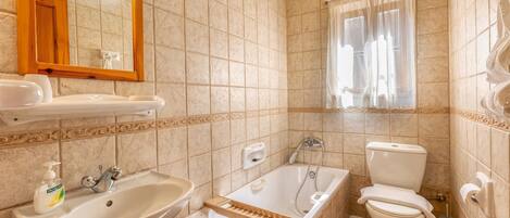 A bathroom with a sink, mirror, bathtub, toilet, and window with curtains.