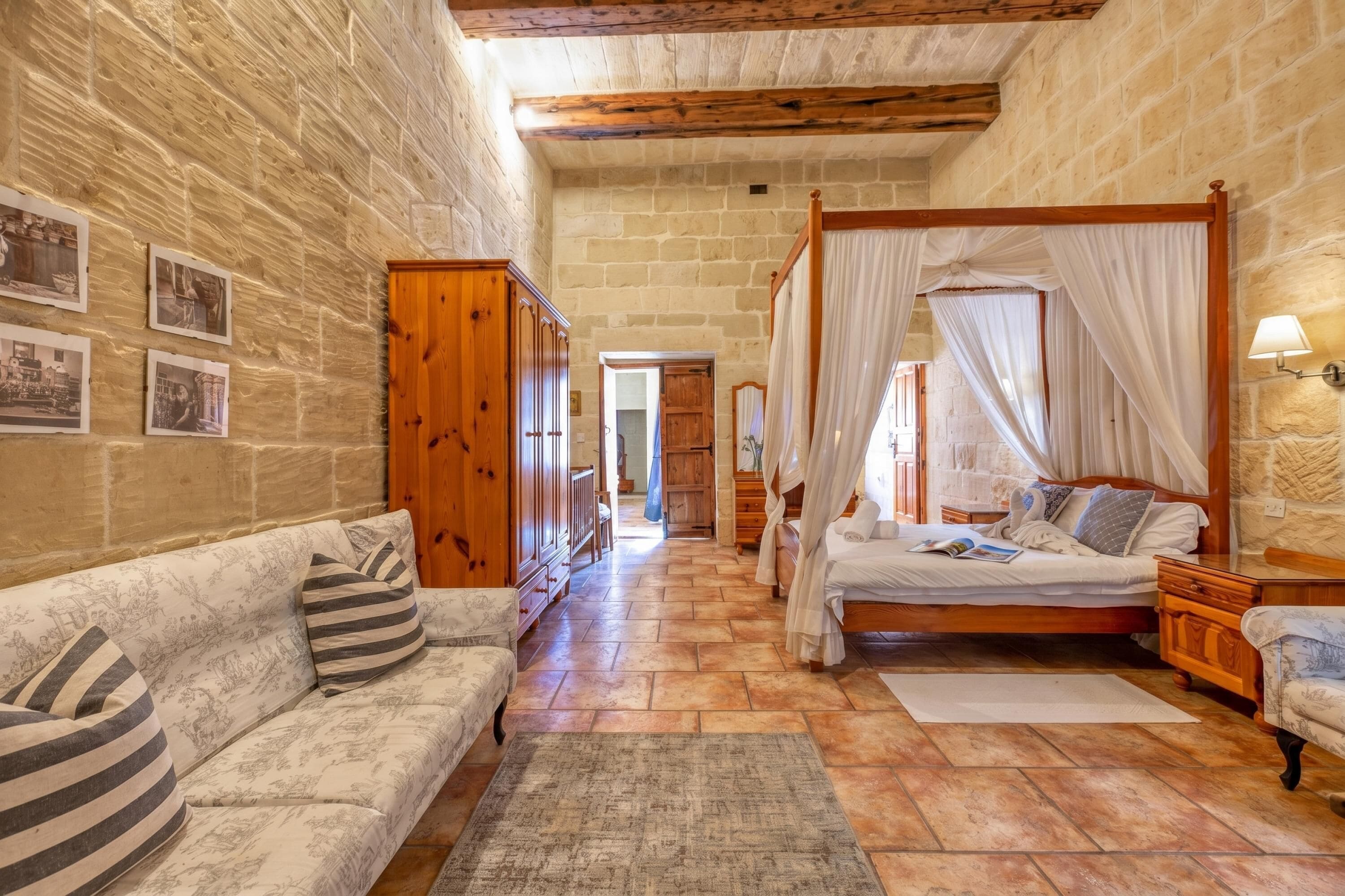 Una camera da letto con un letto a baldacchino, un'armadio in legno, un divano e una parete in pietra.