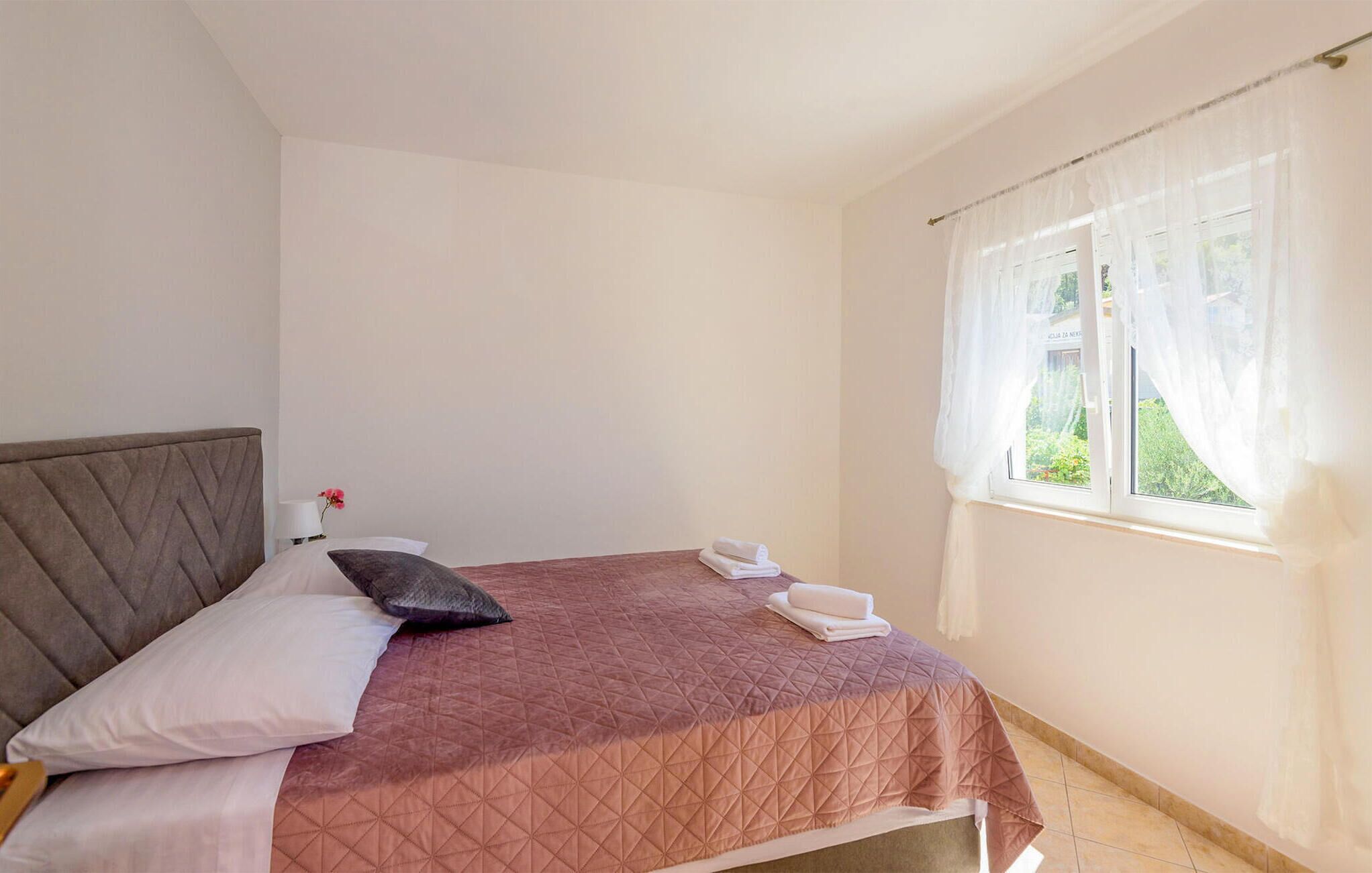 Ein Schlafzimmer mit Bett, Kissen, Nachttisch und einem Fenster mit Vorhängen.