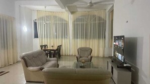 Een woonkamer met een bank, fauteuil, salontafel, televisie en gordijnen.